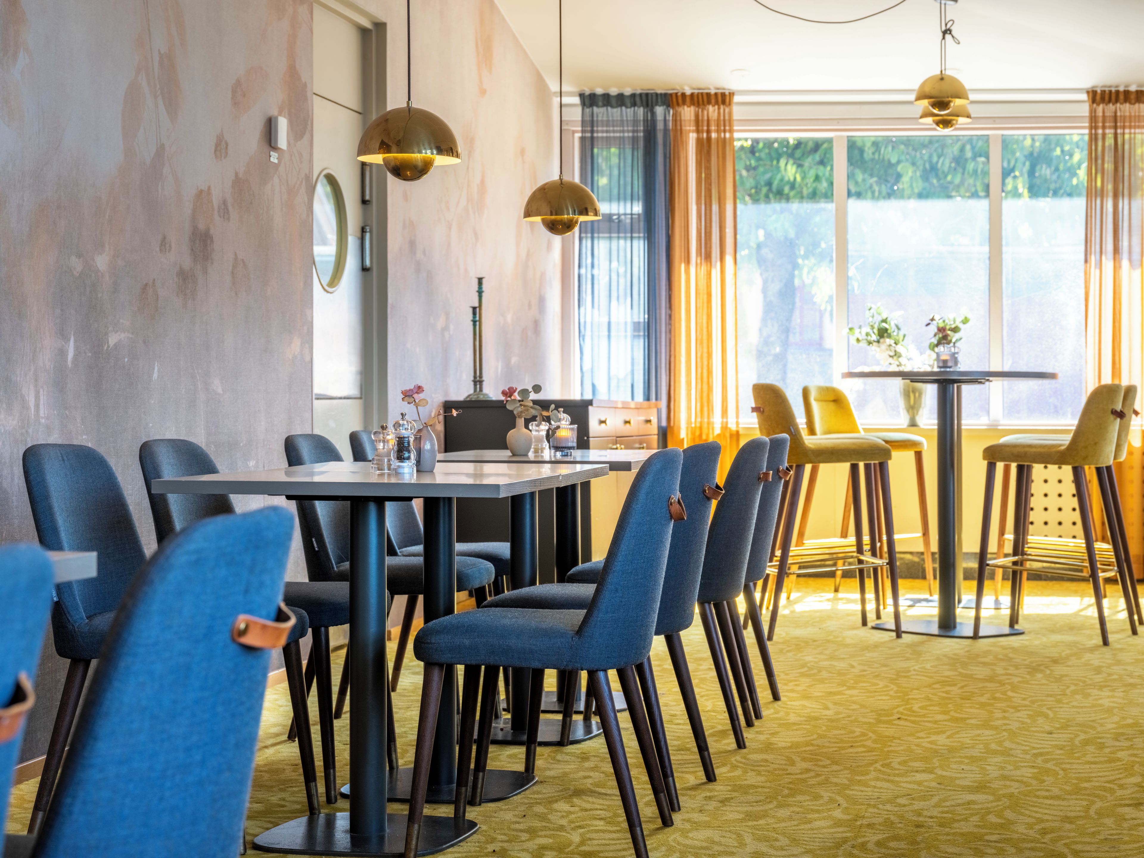 Une salle à manger d’hôtel avec une longue table, des chaises bleues et une petite table ronde avec des chaises jaunes.