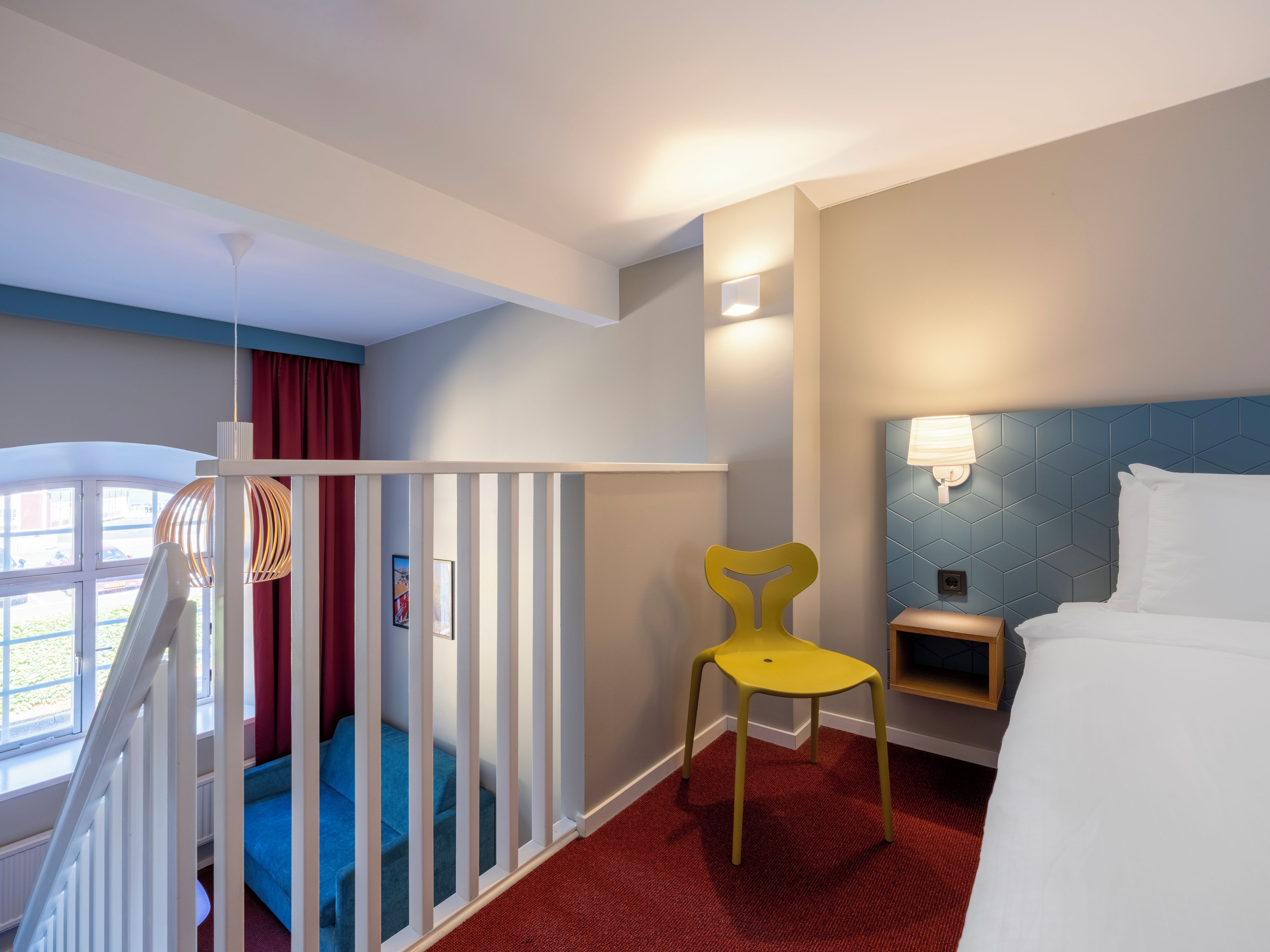 Una habitación de hotel con cama, una silla, un escritorio, un ventanal y una escalera.
