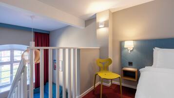 Una habitación de hotel con cama, una silla, un escritorio, un ventanal y una escalera.