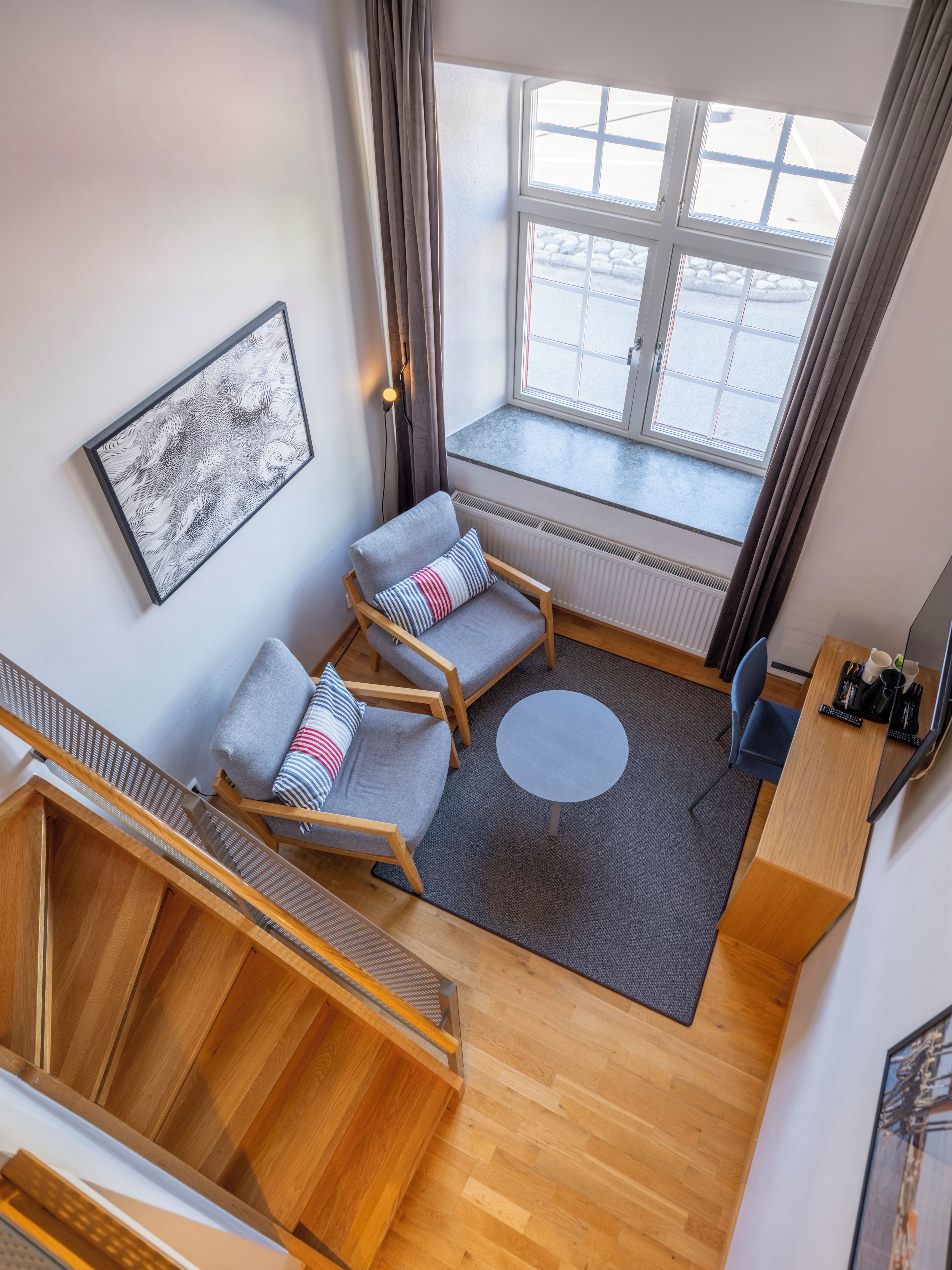 A modern living room with a sofa, chairs, a small table, and a staircase.