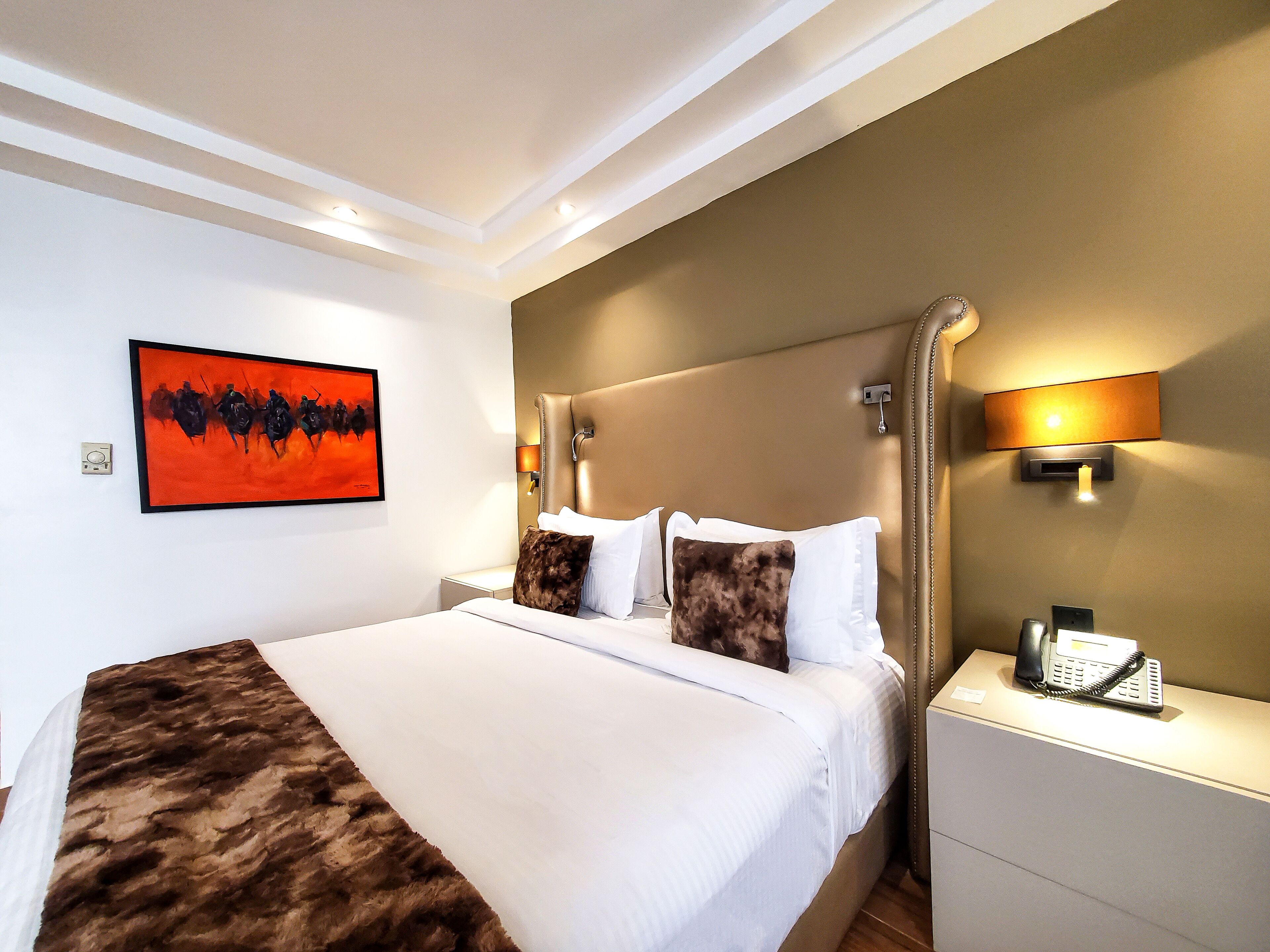 Une chambre d’hôtel dotée d’un grand lit, d’une tête de lit avec éclairage intégré, d’une table de chevet avec un téléphone et d’une œuvre d’art accrochée au mur.