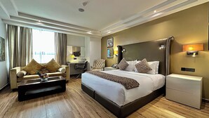 A hotel room with a large bed, a sofa, a desk, and a bedside table. - Victoria Crown Plaza Hotel (Lagos)