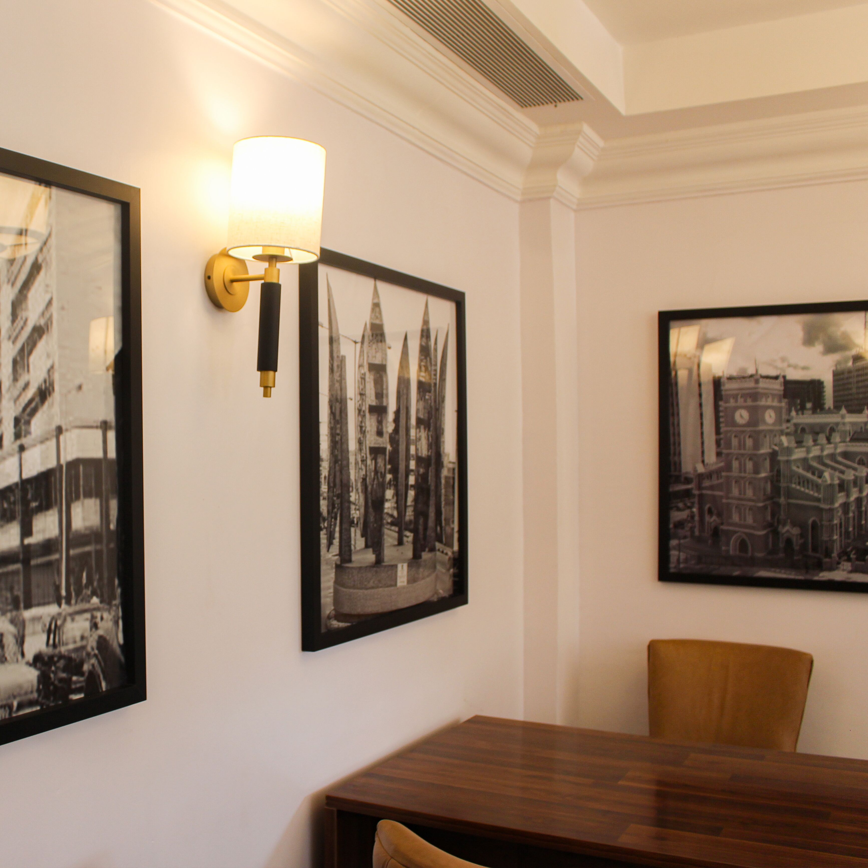 Un comedor con mesa y sillas de madera, fotografías en blanco y negro en la pared y una lámpara de pared.