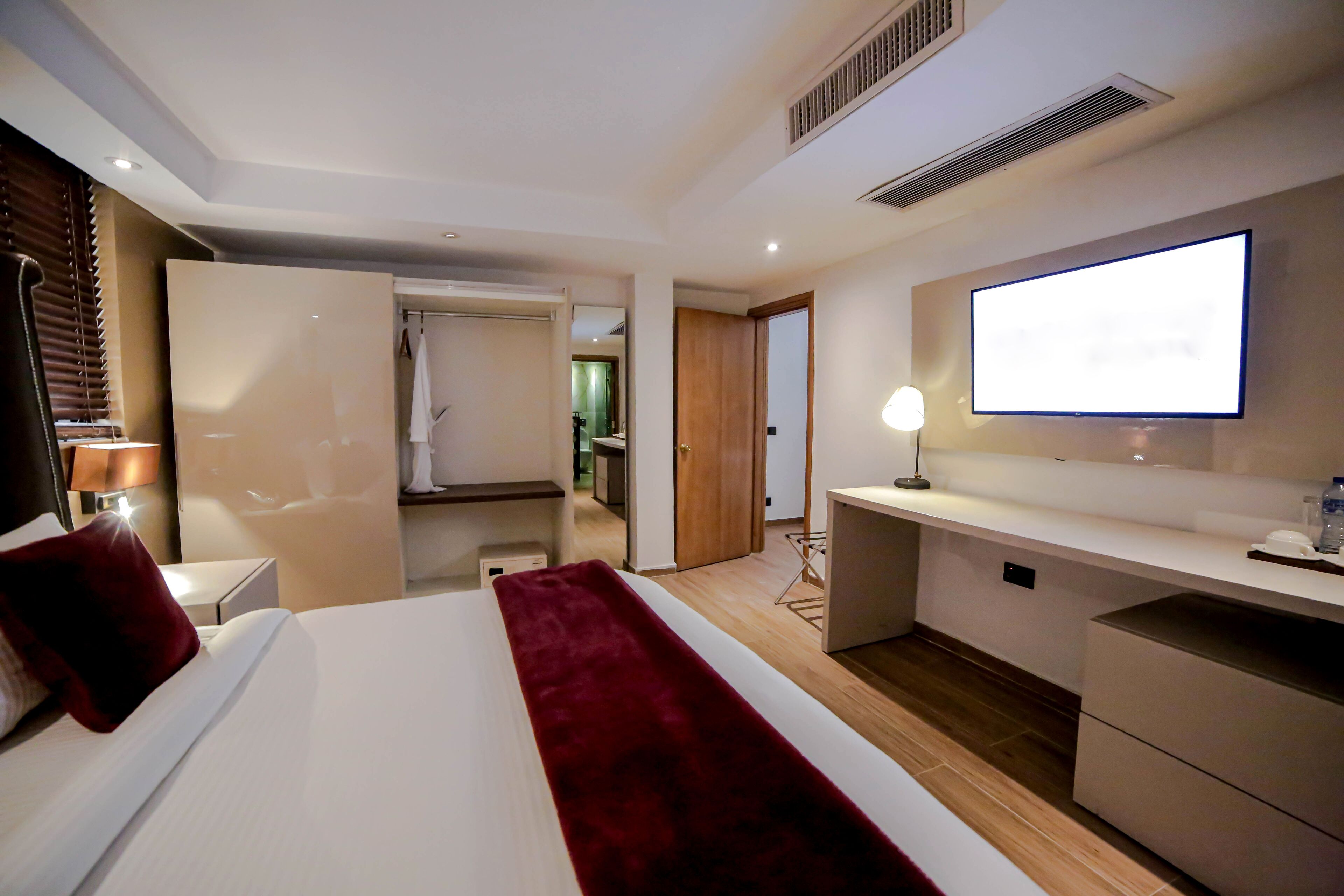 A modern hotel room with a large bed, a desk, a flat-screen TV, and a walk-in closet.