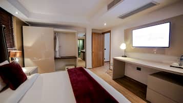 A modern hotel room with a large bed, a desk, a flat-screen TV, and a walk-in closet.