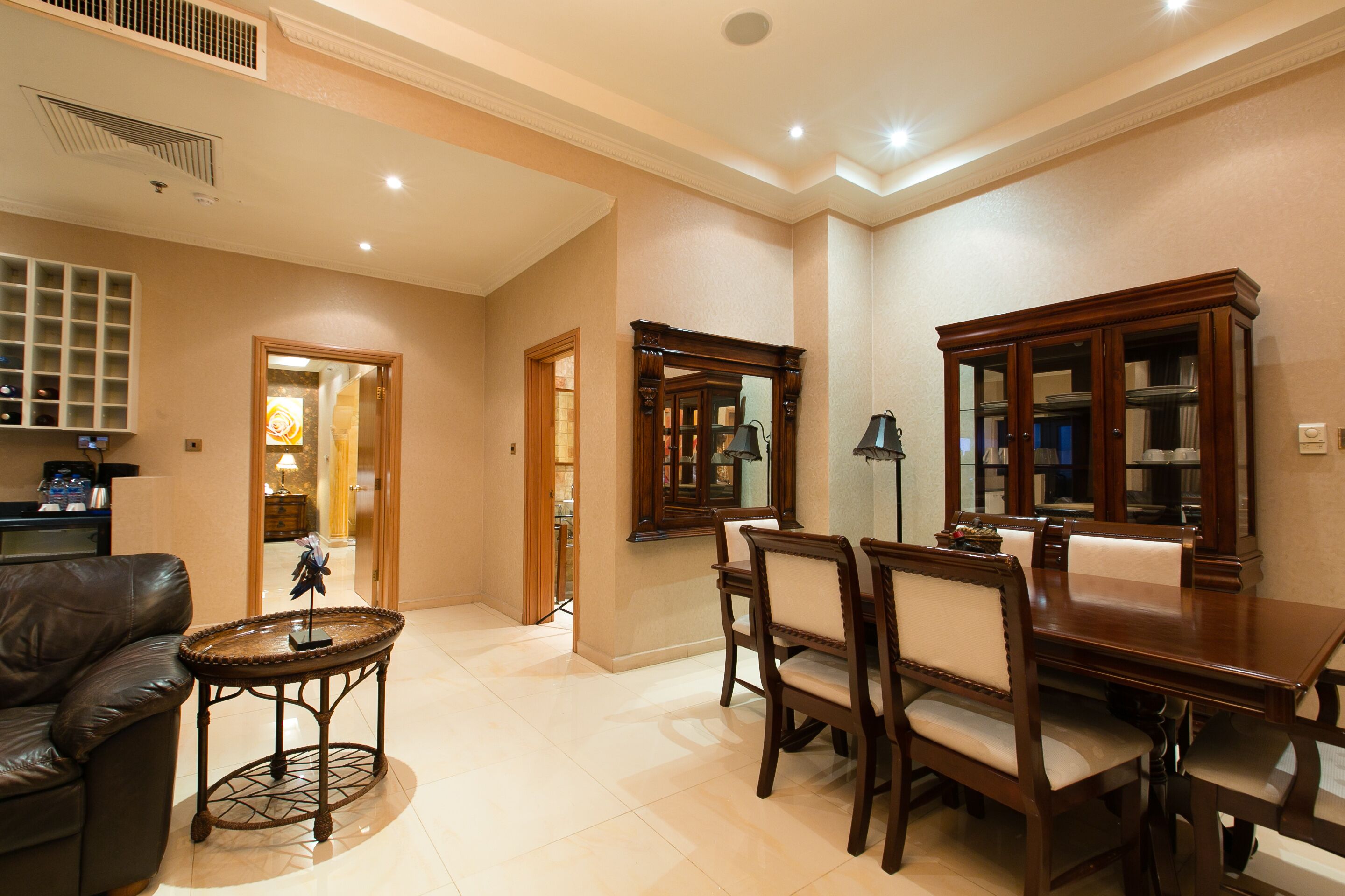 A spacious living room with a dark leather sofa, a round coffee table, and a dining area with wooden chairs and a table.