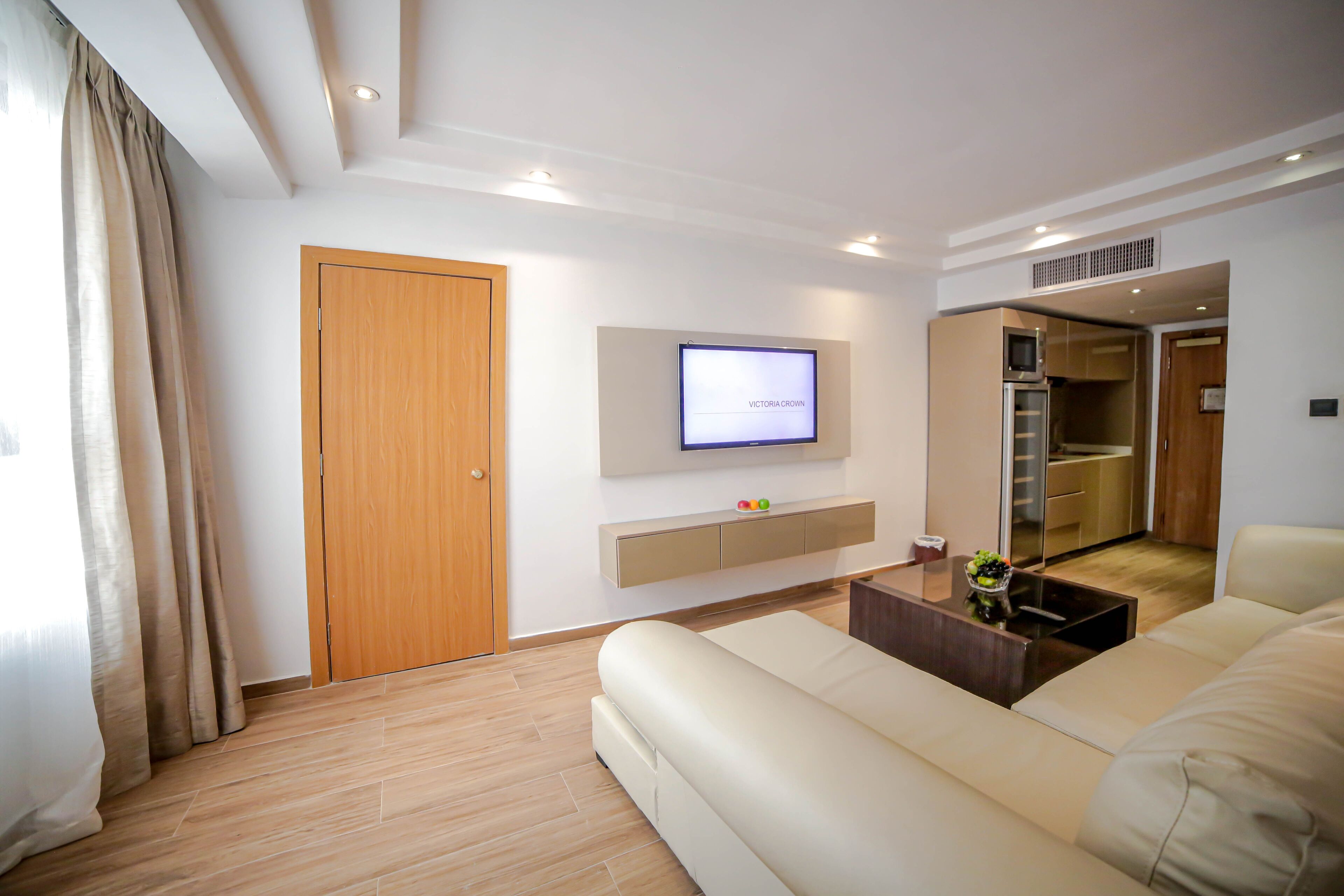A modern living room with a flat-screen TV, a sofa, a coffee table, and a wooden door.