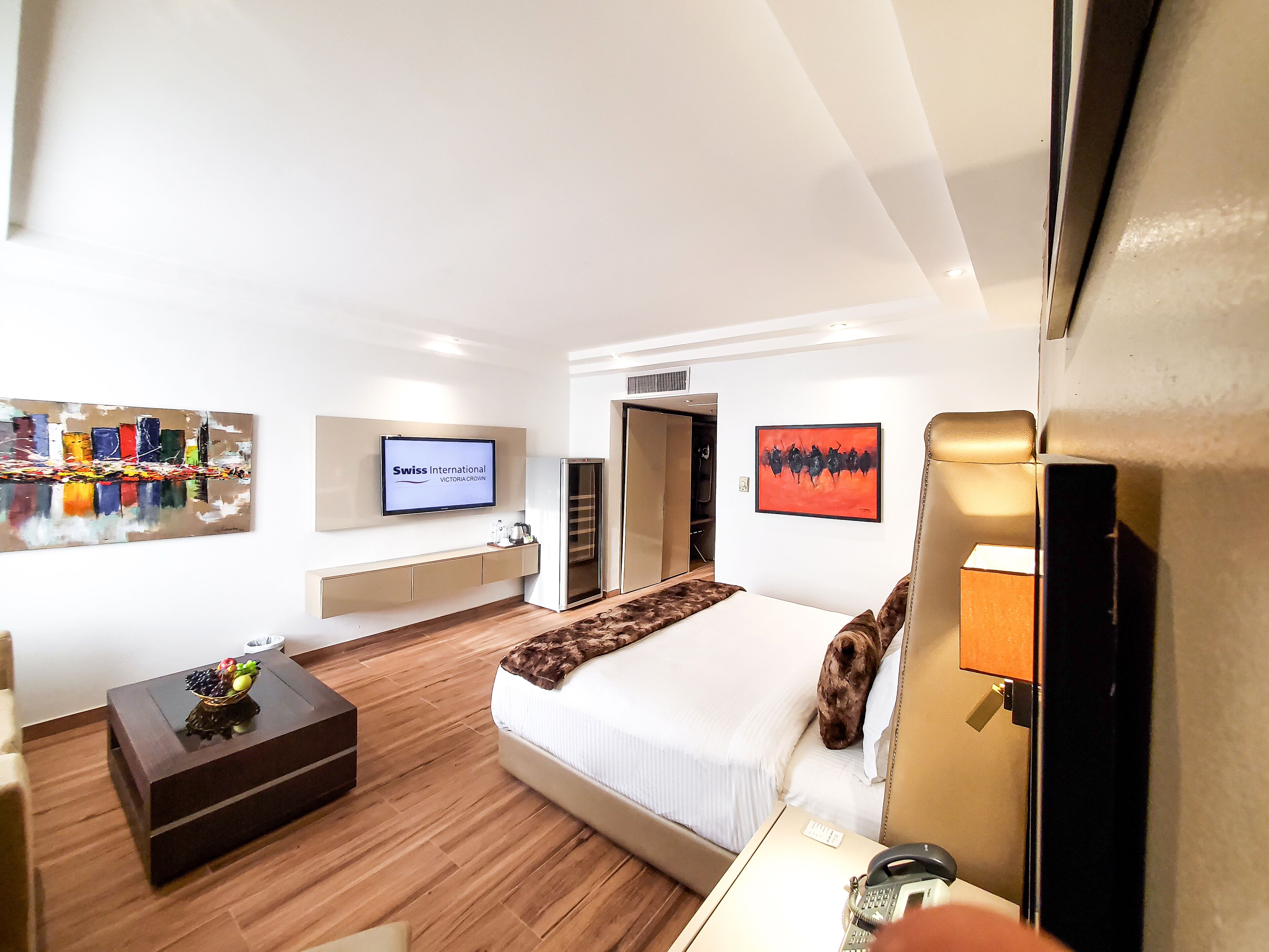 Ein Hotelzimmer mit Bett, Nachttisch, Fernseher, Kunstwerk und einer Minibar.