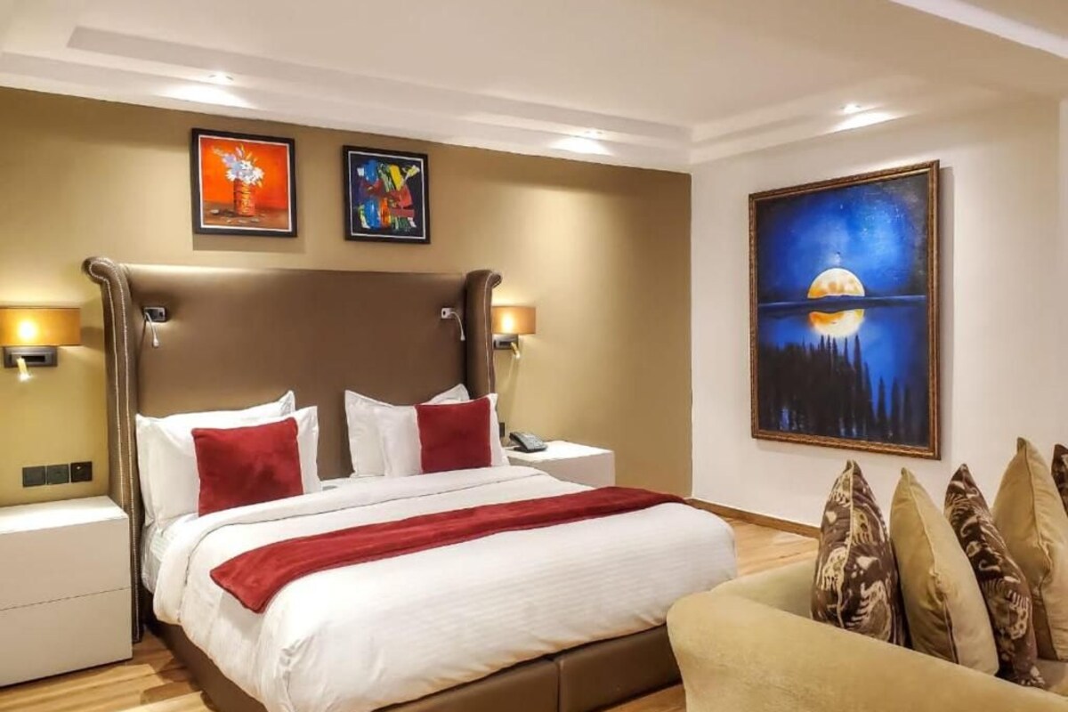 Una habitación de hotel con una cama grande, mesitas de noche, un sofá y obras de arte en las paredes.