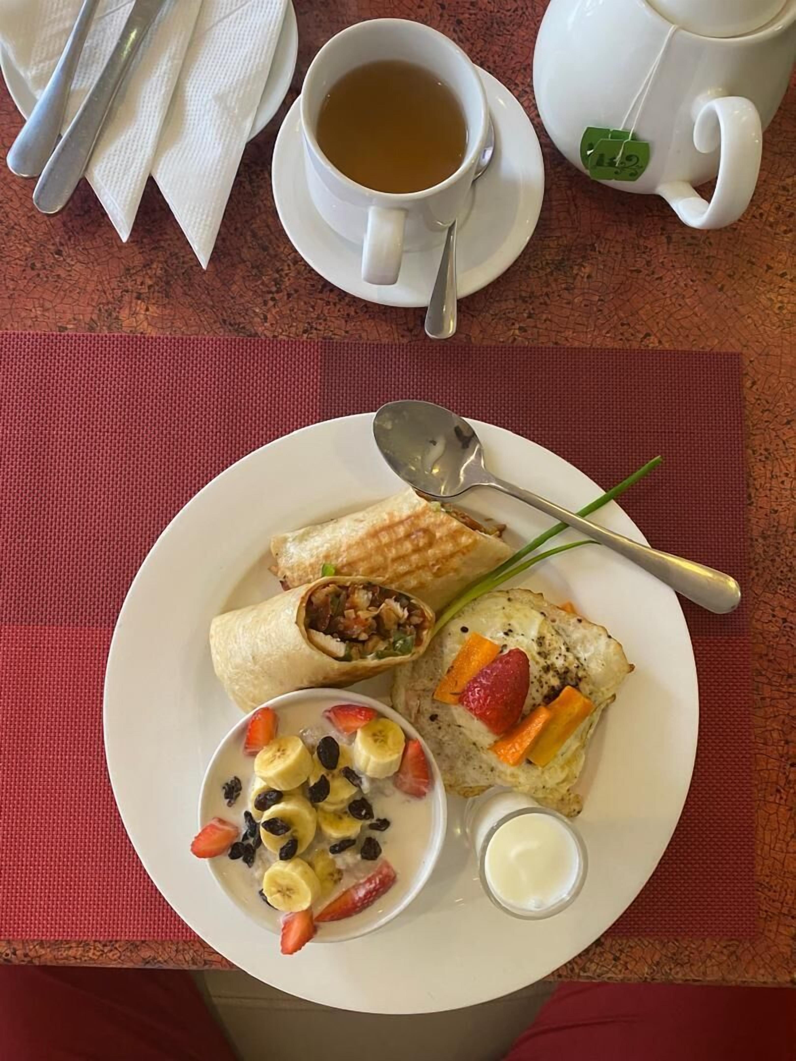 Une assiette de petit-déjeuner comprenant un wrap, un assortiment de fruits et une tasse de thé.