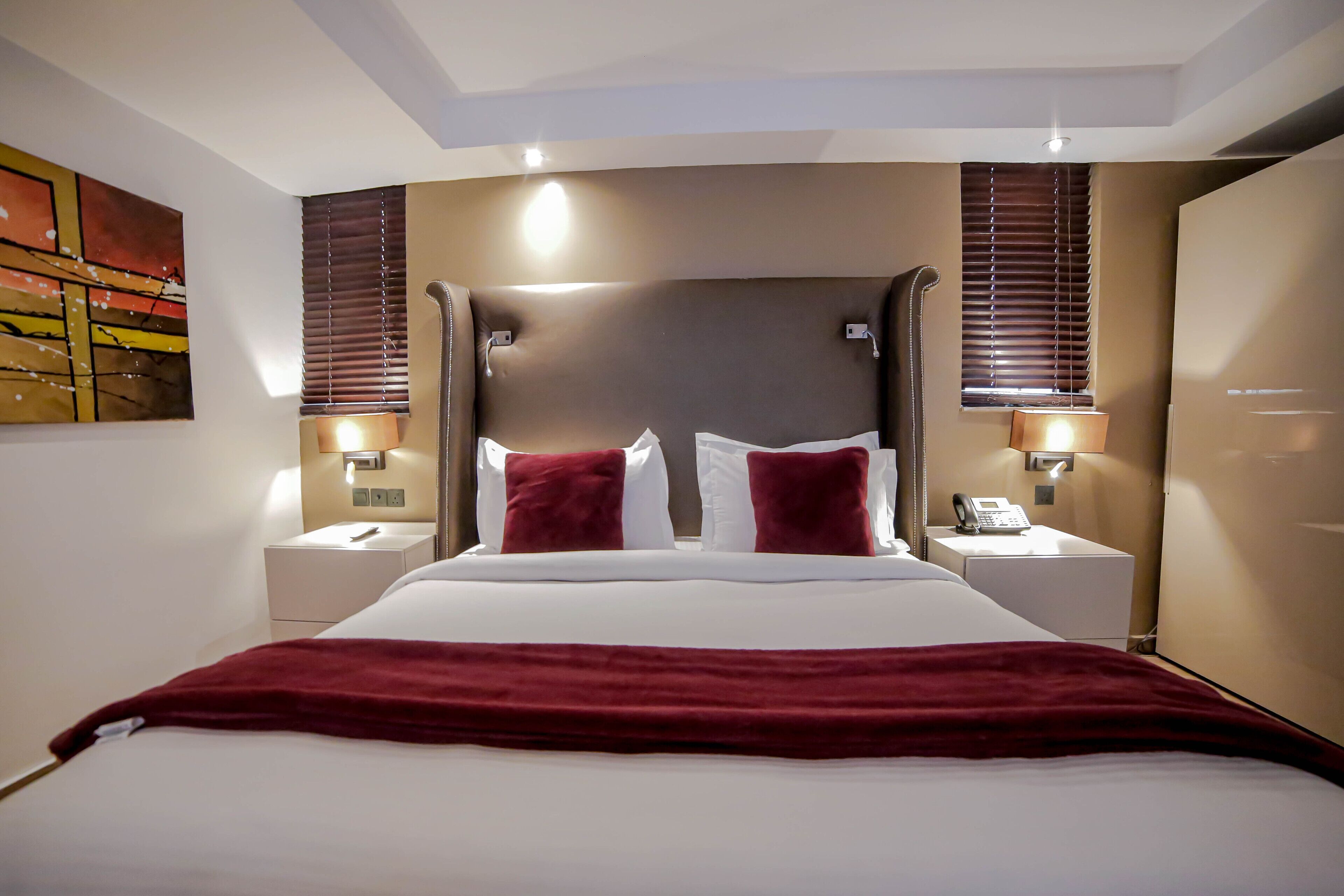 Een hotelkamer met een groot bed, twee nachtkastjes, een telefoon en een schilderij aan de muur.