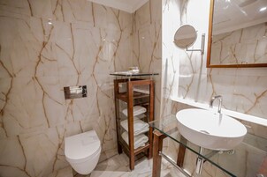 A bathroom with a marble wall, a glass sink, a wooden towel rack, and a toilet.