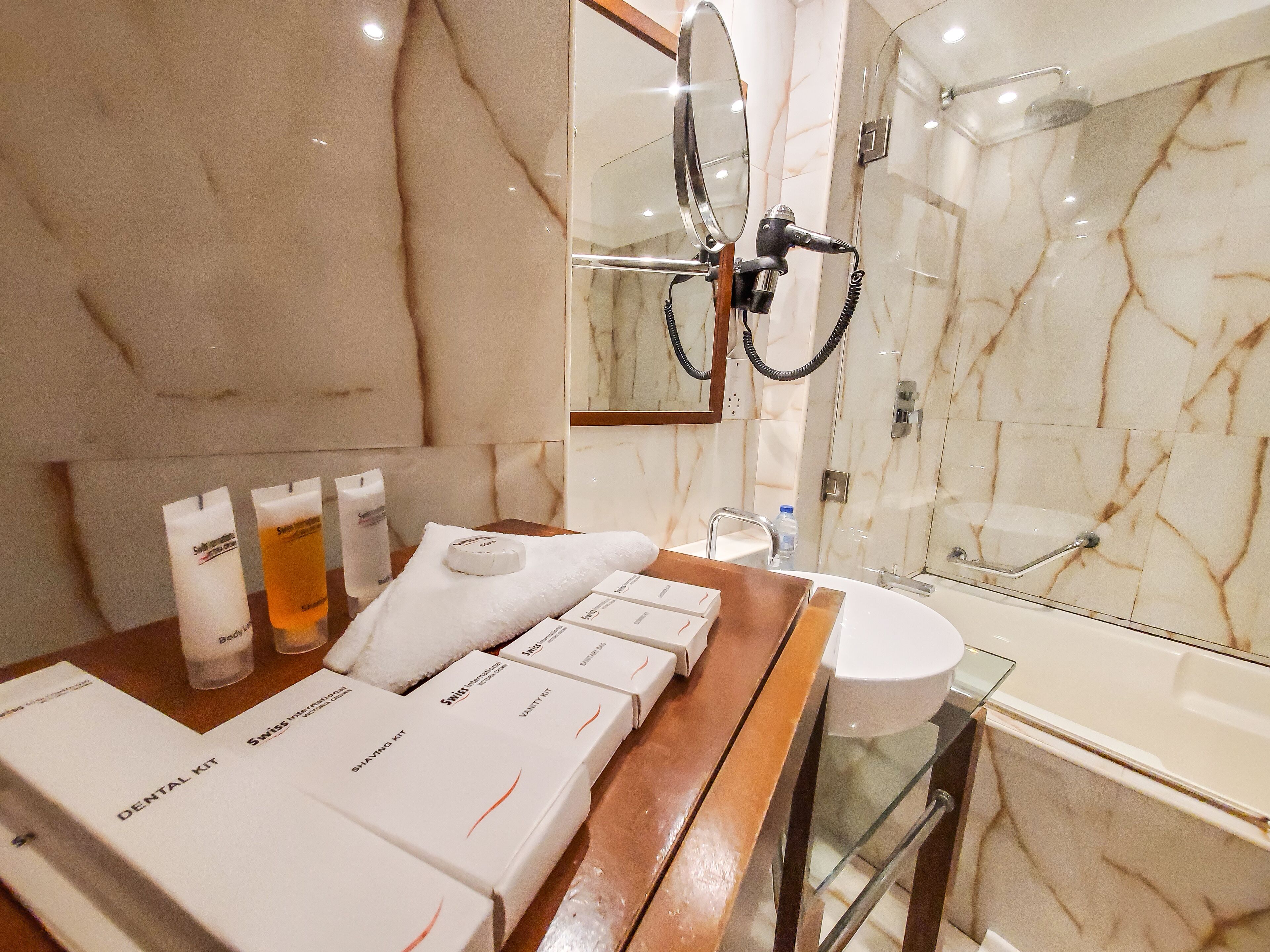 A bathroom with a marble wall, a wooden vanity, a sink, a mirror, and a shower.