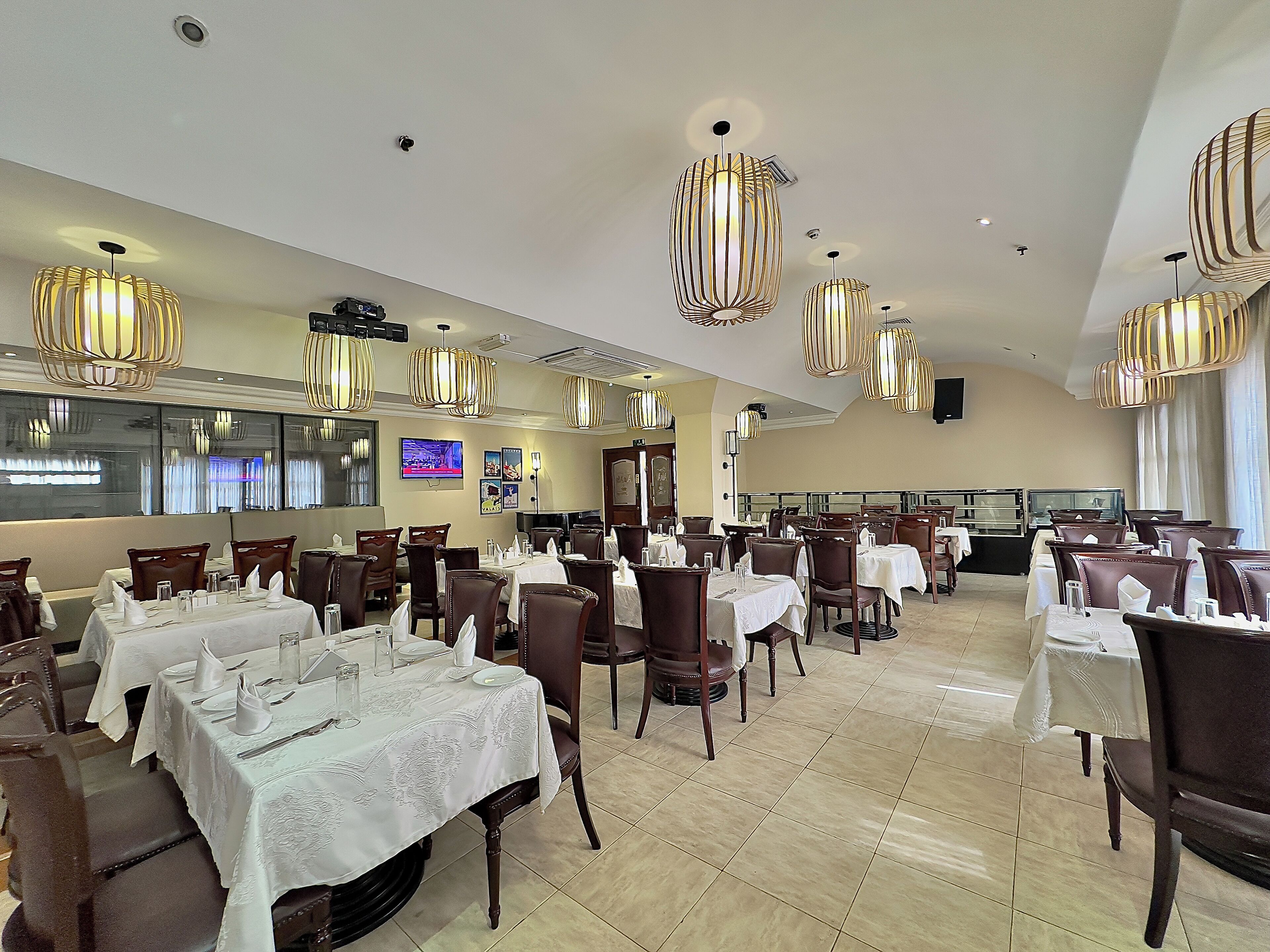 A spacious dining area with multiple tables and chairs, decorative lighting, and a television screen on the wall.