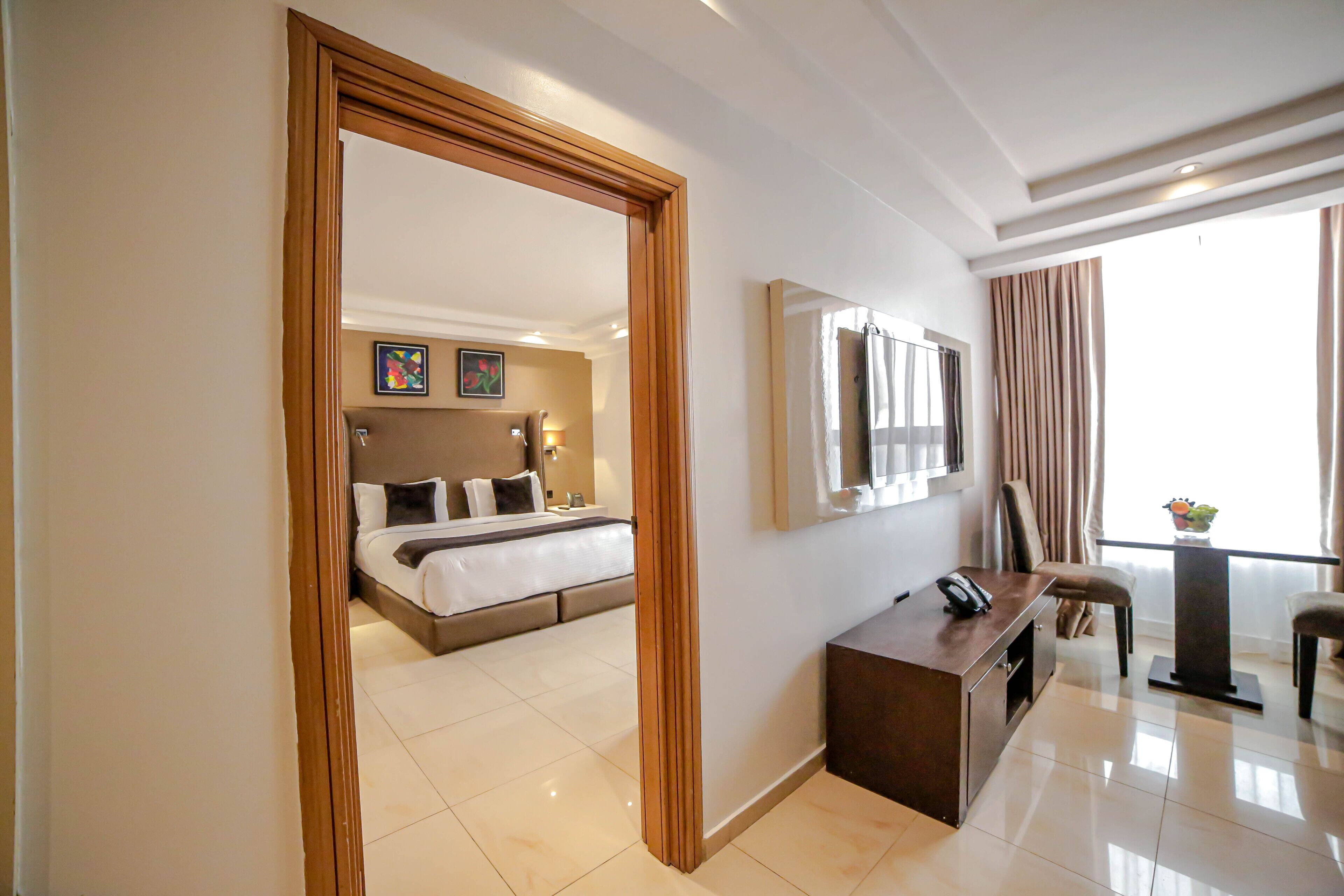 A hotel room with a bed, bedside table, TV, and a balcony with curtains.