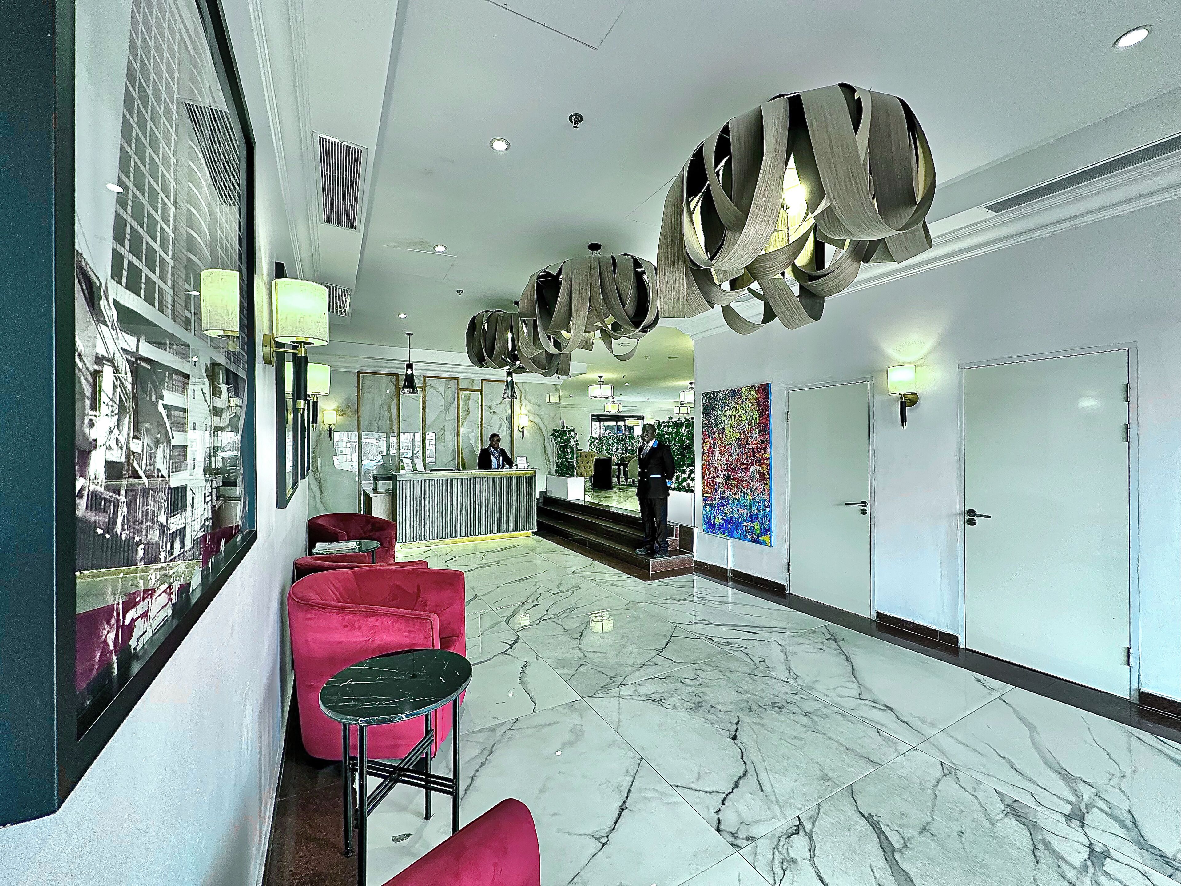 A hotel lobby with a reception desk, red seating, a marble floor, and modern ceiling fixtures.