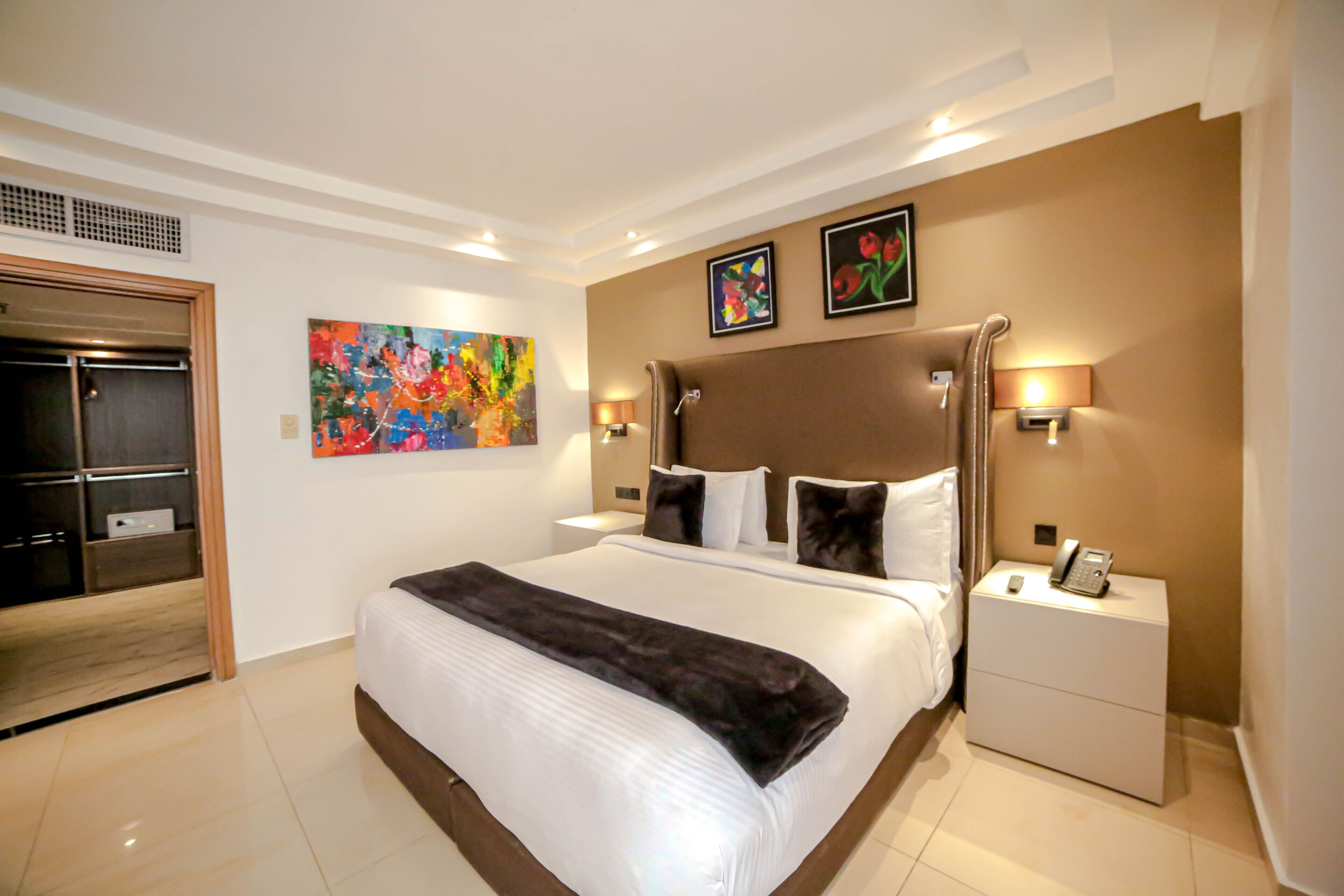 Hotelkamer met een groot bed, nachtkastje met telefoon, schilderij aan de muur en deur naar een inloopkast.