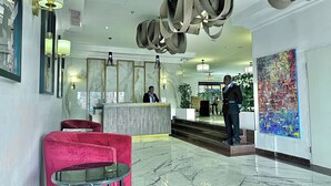 A hotel lobby with a reception desk, a red chair, a glass table, and a large abstract painting. - Victoria Crown Plaza Hotel (Lagos)