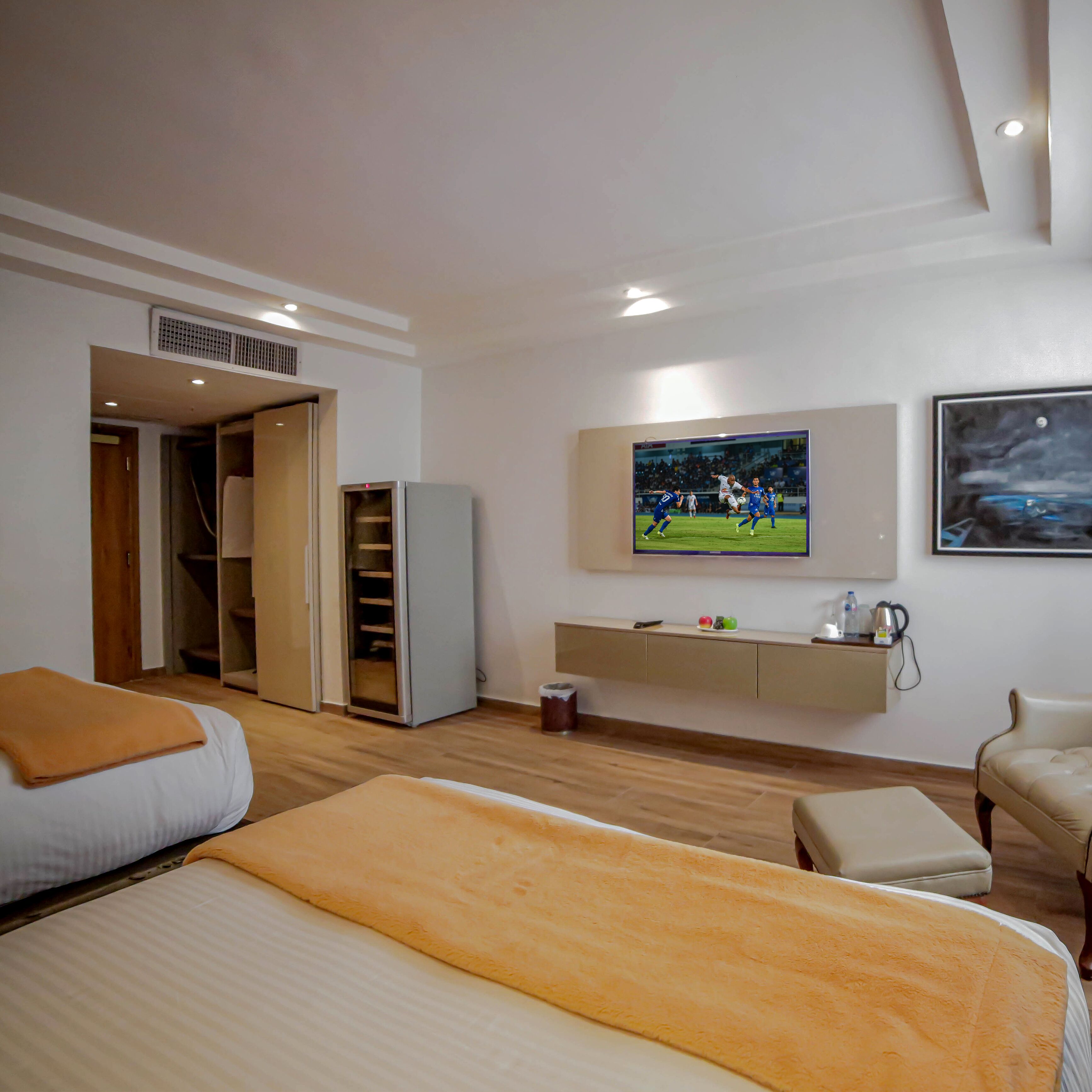 A hotel room with a bed, a seating area, a TV mounted on the wall, and a kitchenette.