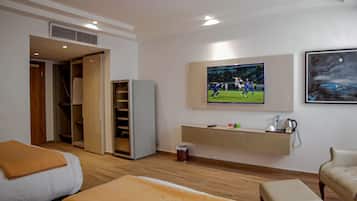 A hotel room with a bed, a seating area, a TV mounted on the wall, and a kitchenette.