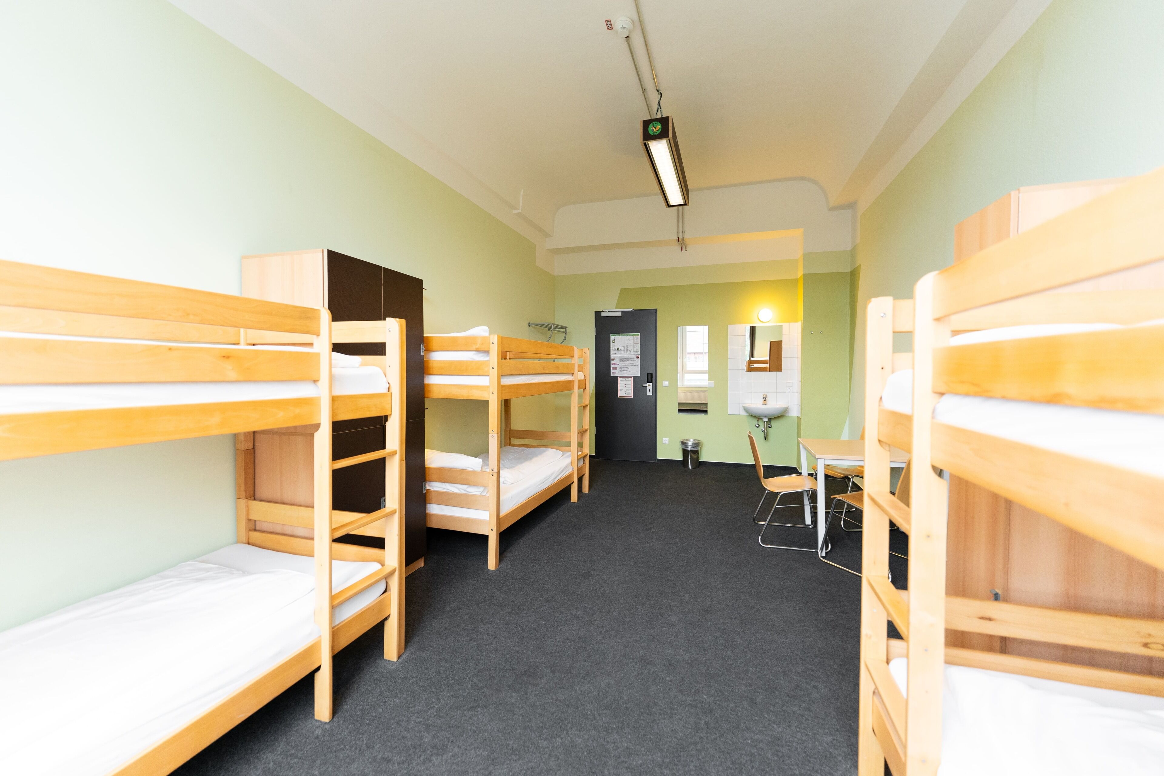 Ein Schlafsaalzimmer mit Etagenbetten, einem Schreibtisch und einem Spiegel.