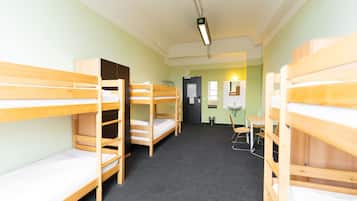 Ein Schlafsaalzimmer mit Etagenbetten, einem Schreibtisch und einem Spiegel.