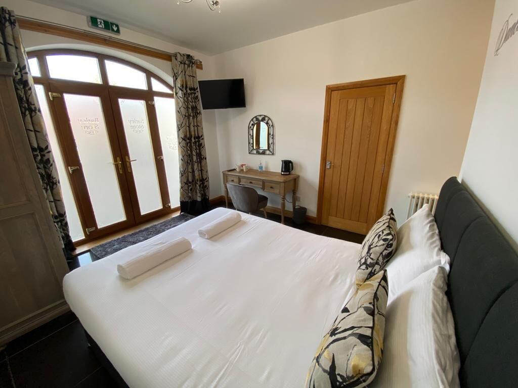 A hotel room with a large bed, a desk with a chair, a television, and a wooden door.