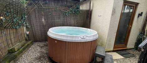 A hot tub in a backyard with a wooden fence, a door, and a small deck.