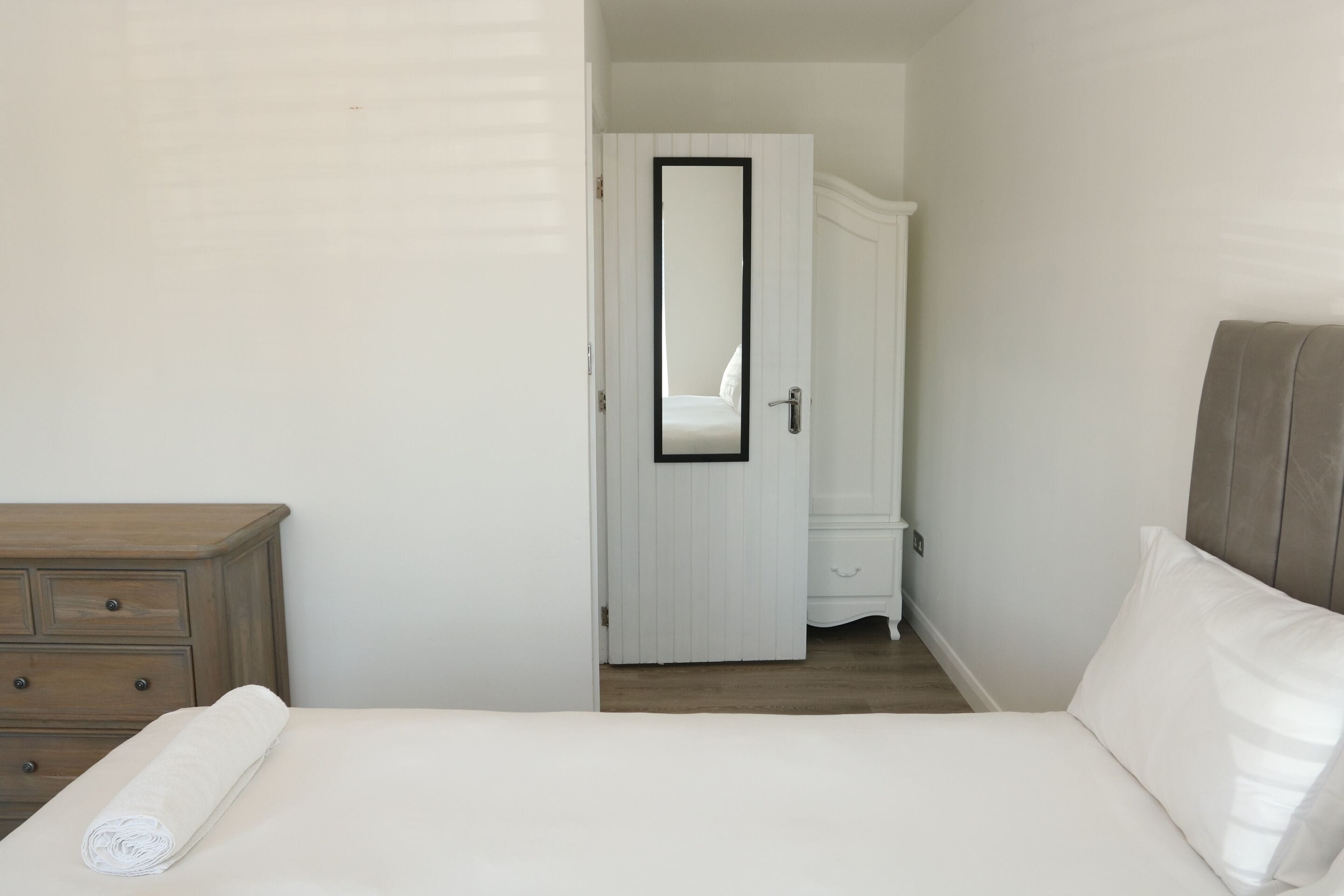Un dormitorio con una cama, un aparador de madera y un armario blanco.
