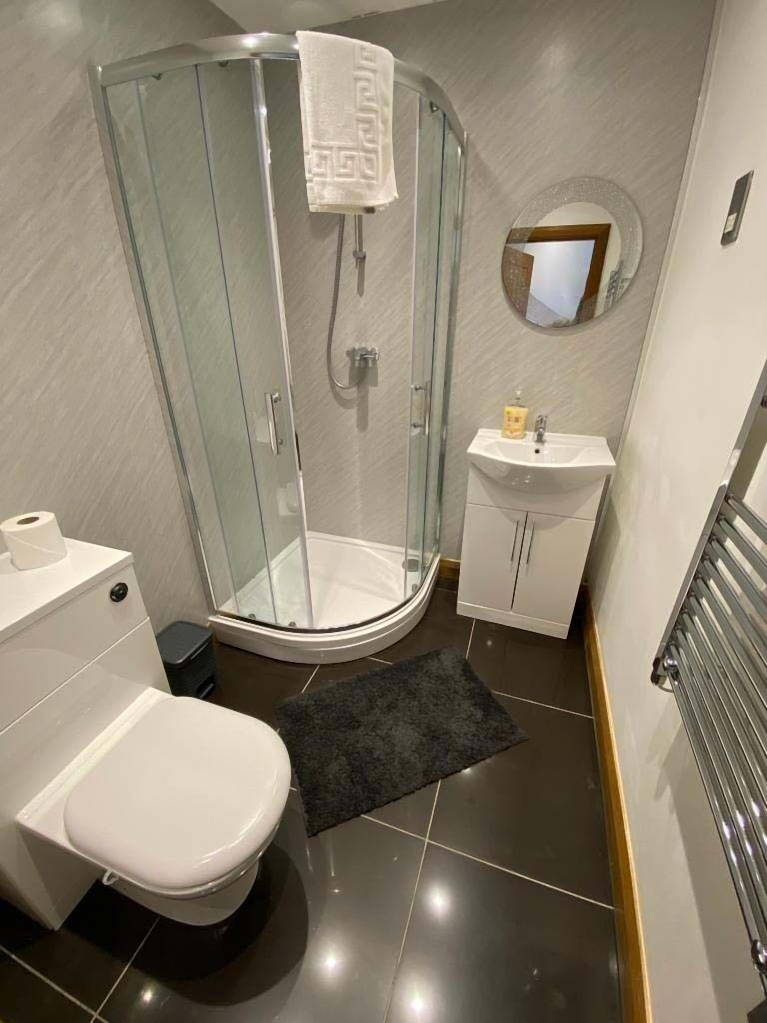 Une salle de bain moderne dotée d’une douche à parois de verre, de toilettes, d’un lavabo et d’un miroir.