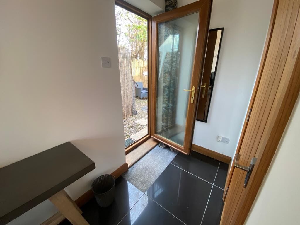 A room with a sliding glass door leading to a patio, a small trash bin, and a wooden bench.