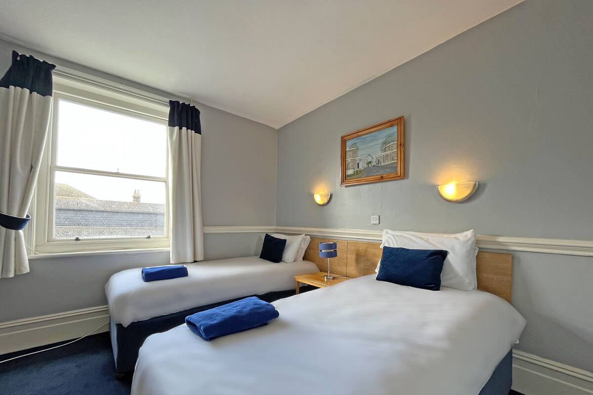 Habitación de hotel con dos camas, una ventana con cortinas, un cuadro en la pared y dos luces fijadas a la pared.
