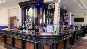 Een bar met een donker houten toonbank, een klok en verschillende flessen en glazen.