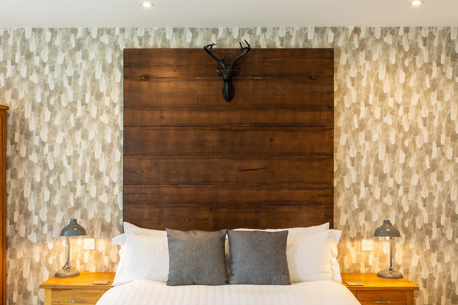 A bedroom with a wooden headboard, two bedside lamps, and a bed with white and gray pillows.