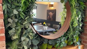 A mirror surrounded by lush greenery, a fireplace below, and a dining area in the background. - The Royal Oak - Inn (Loughborough)