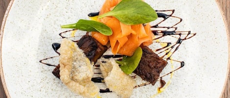 A plate with various food items including a piece of meat, a carrot, and a leafy green, arranged on a speckled ceramic plate.