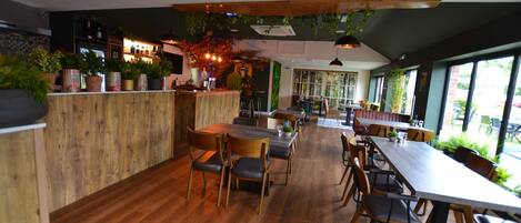 A restaurant with wooden flooring, a bar area, and large windows allowing natural light.