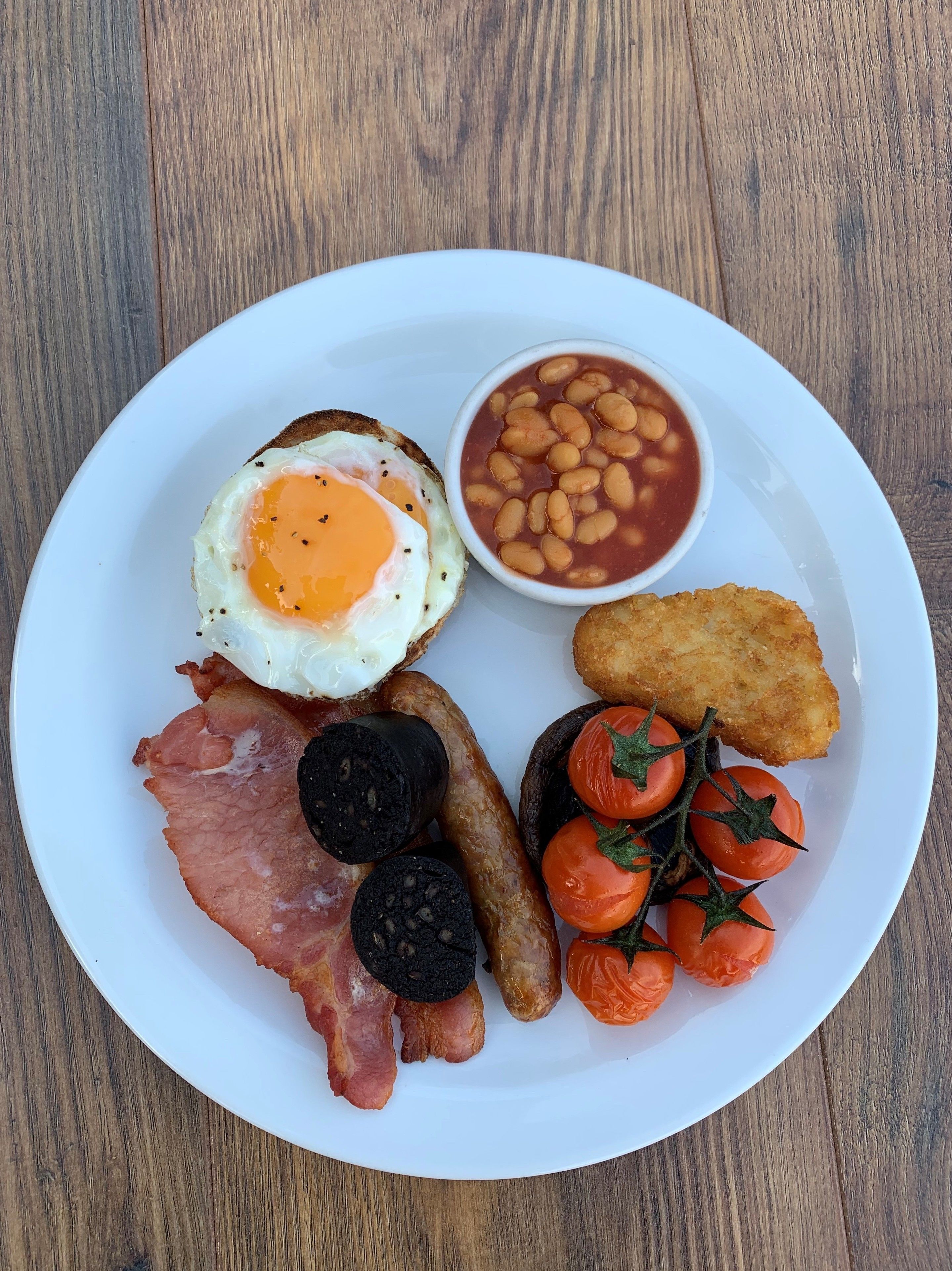Ein Teller mit Frühstücksessen, darunter Eier, Bohnen, Speck, Würstchen und Tomaten.
