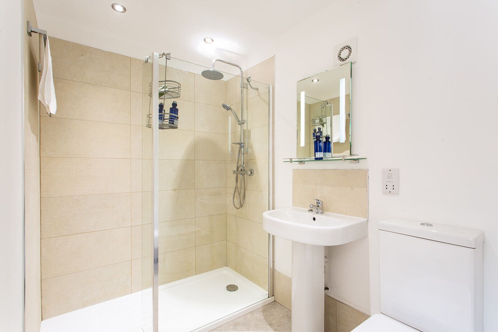 Un baño moderno con ducha de vidrio, lavamanos pedestal y tocador con espejo.