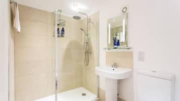 Un baño moderno con ducha de vidrio, lavamanos pedestal y tocador con espejo.