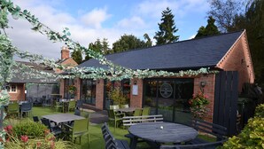 An outdoor seating area with tables and chairs, a brick building, and greenery. - The Royal Oak - Inn (Loughborough)