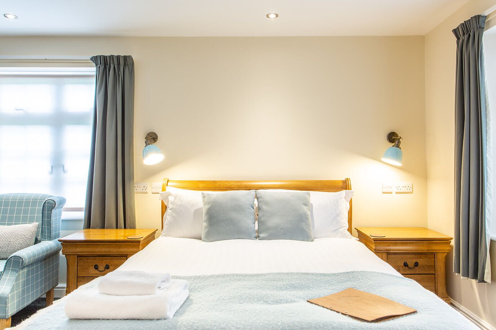 Una camera d'albergo con un letto grande, due comodini, una sedia e una finestra con tende.
