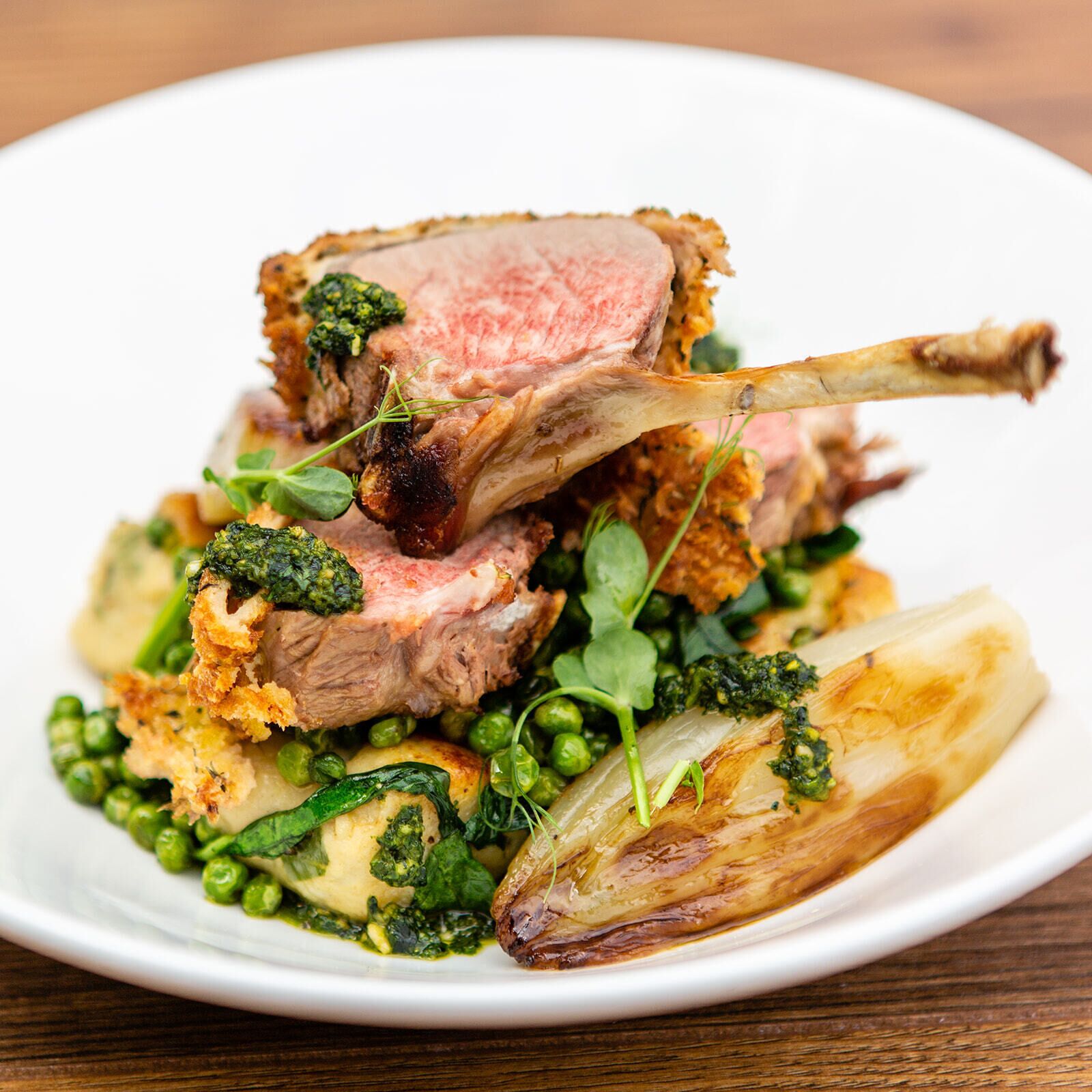 Un piatto con una costoletta d'agnello, piselli e verdure a foglia verde.
