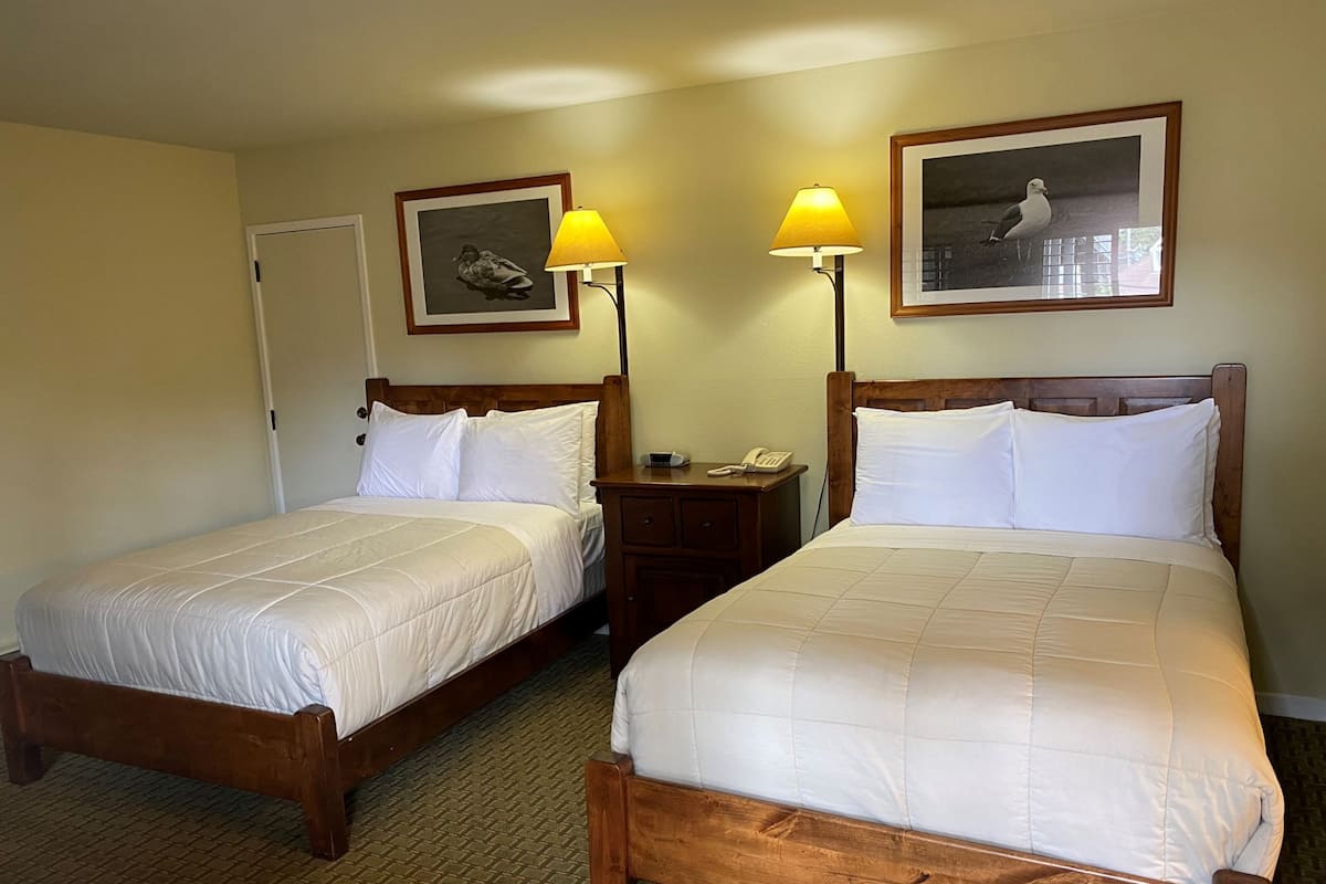 Two single beds with wooden frames and white bedding, a nightstand with a lamp, and framed pictures on the wall.