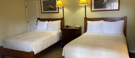 Two single beds with wooden frames and white bedding, a nightstand with a lamp, and framed pictures on the wall.