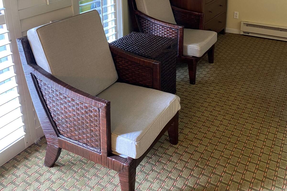A room with a wicker chair, a small table, and a TV mounted on the wall.