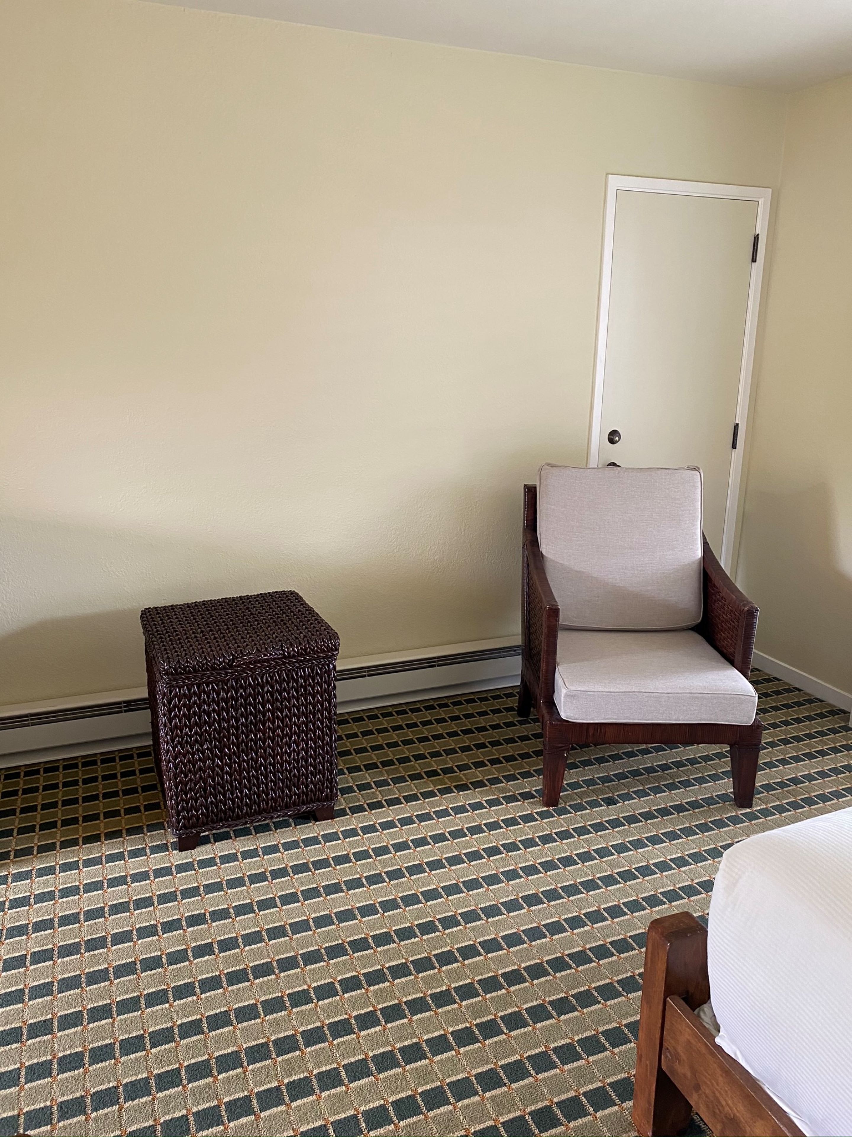 Una habitación con piso estampado, una silla de madera con cojín, un taburete pequeño de mimbre y una puerta blanca.