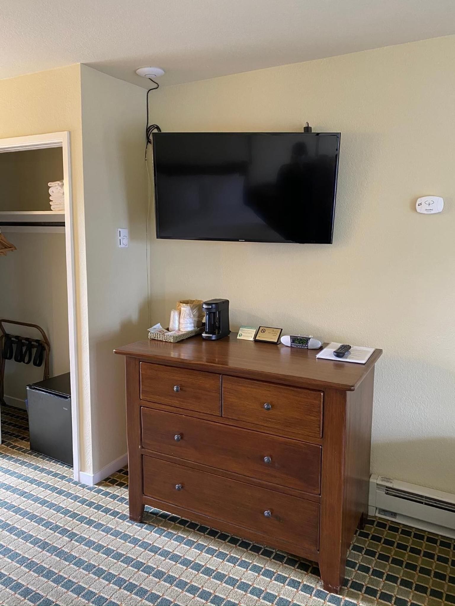 Hotelkamer met een flatscreen televisie aan de muur, een houten dressoir met lades, een koffiezetapparaat en een klein bordje.