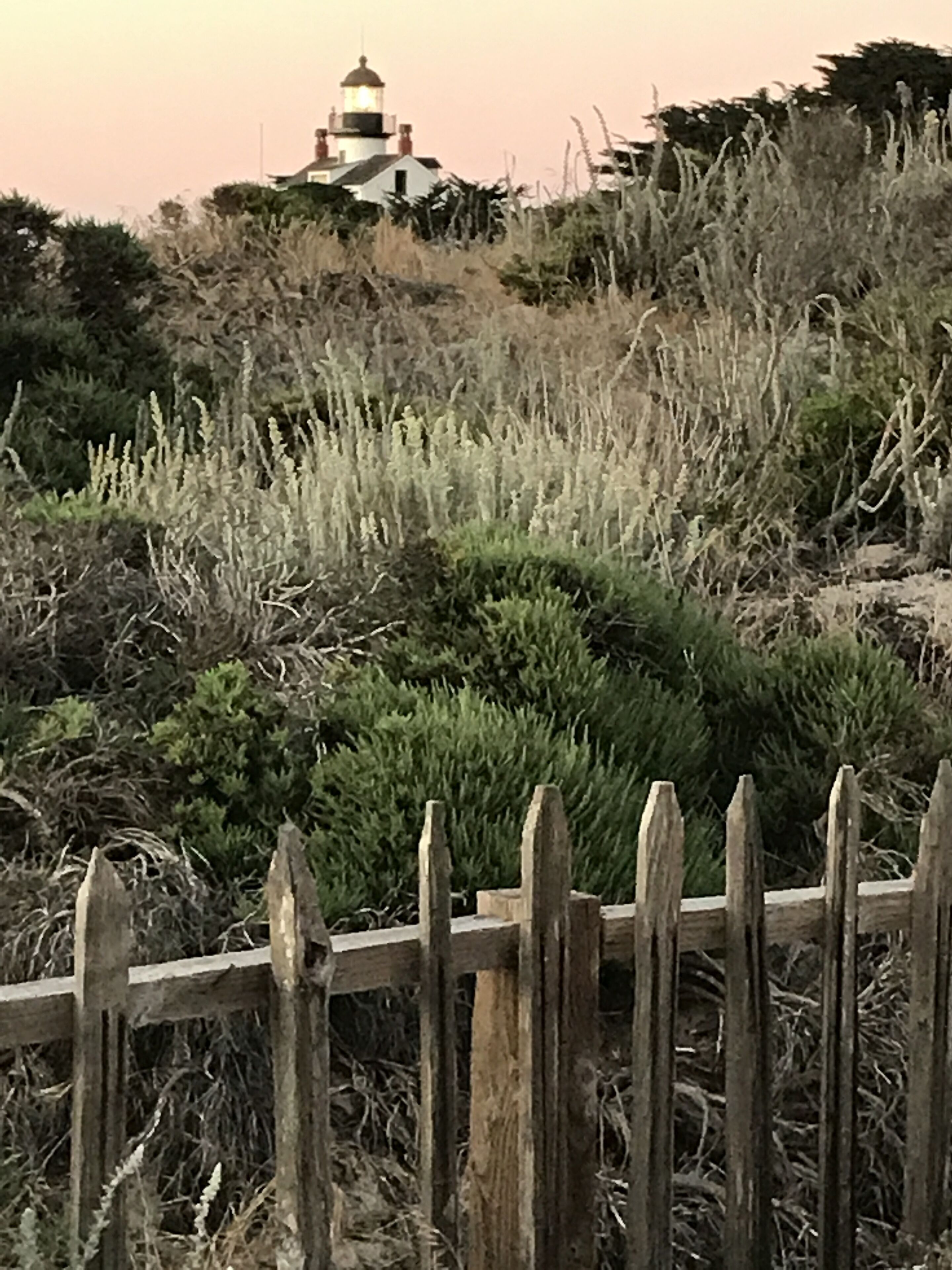 A lighthouse on a hill with a wooden fence in the foreground.