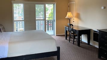 A hotel room with a large bed, a desk with a chair, a lamp, and a view through the window.